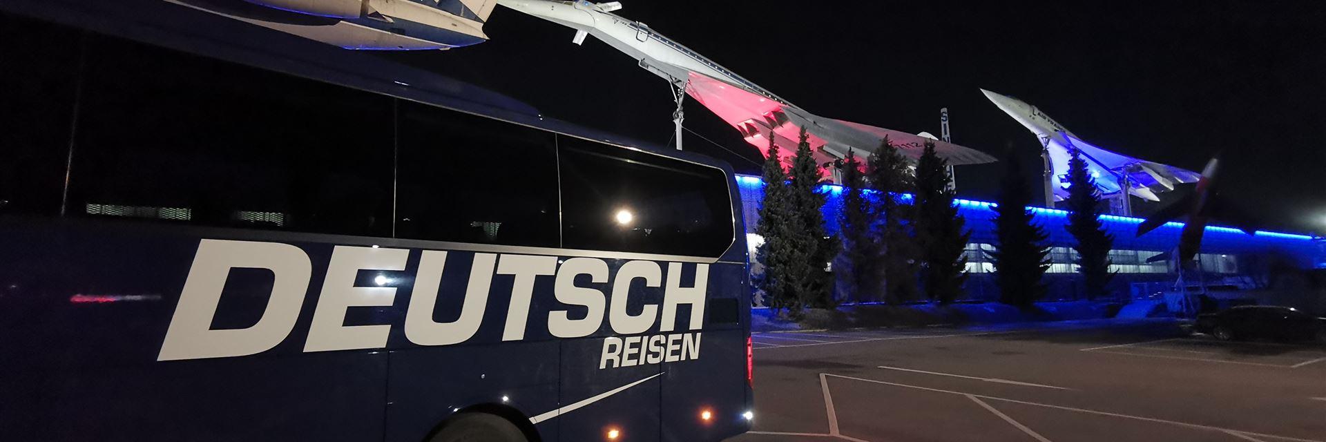 blauer Reisebus vor einem Flugzeug bei Nacht