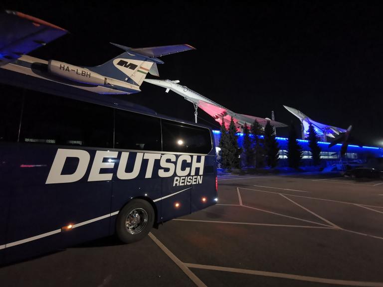 blauer Reisebus vor einem Flugzeug bei Nacht