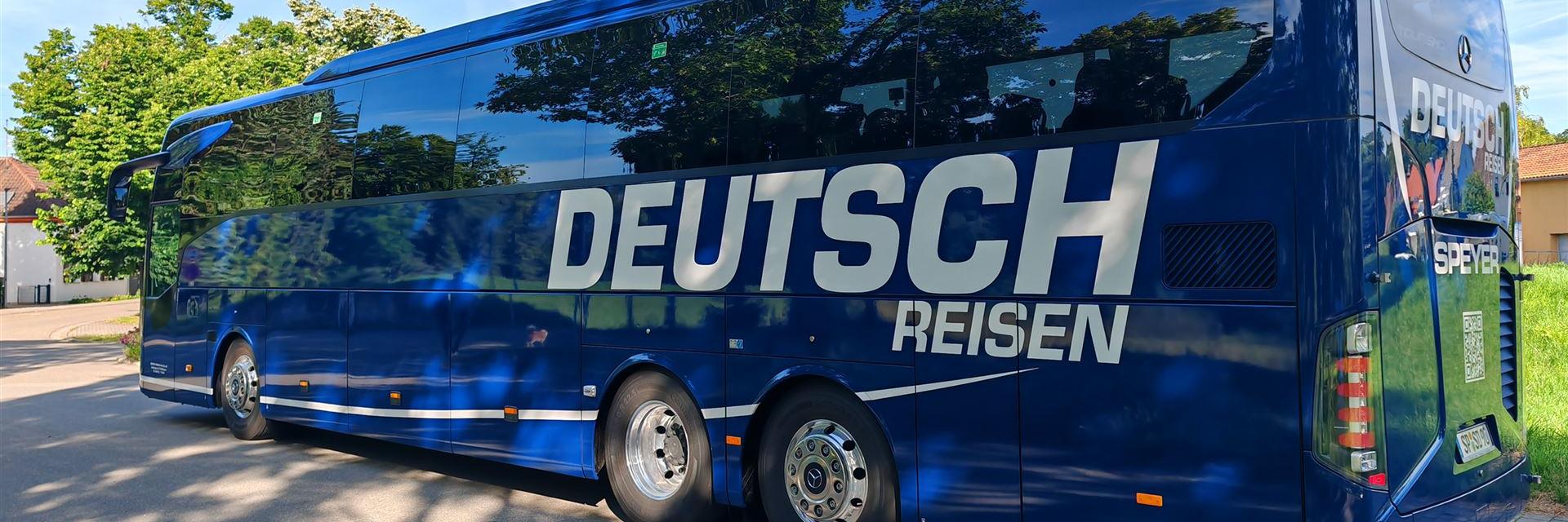 blauer Reisebus vor blauem Himmel mit Aufschrift Deutsch