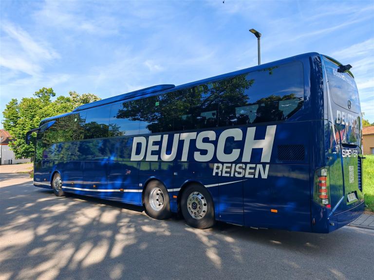 blauer Reisebus vor blauem Himmel mit Aufschrift Deutsch