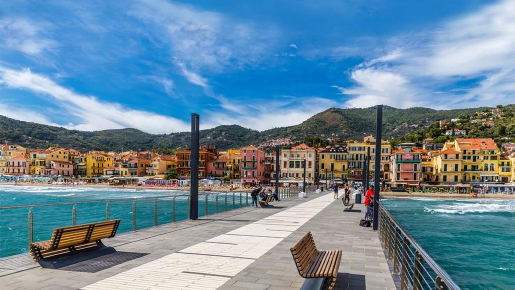 Blumenriviera_Alassio, Brücke mit Bank und Blumen über dem Wasser