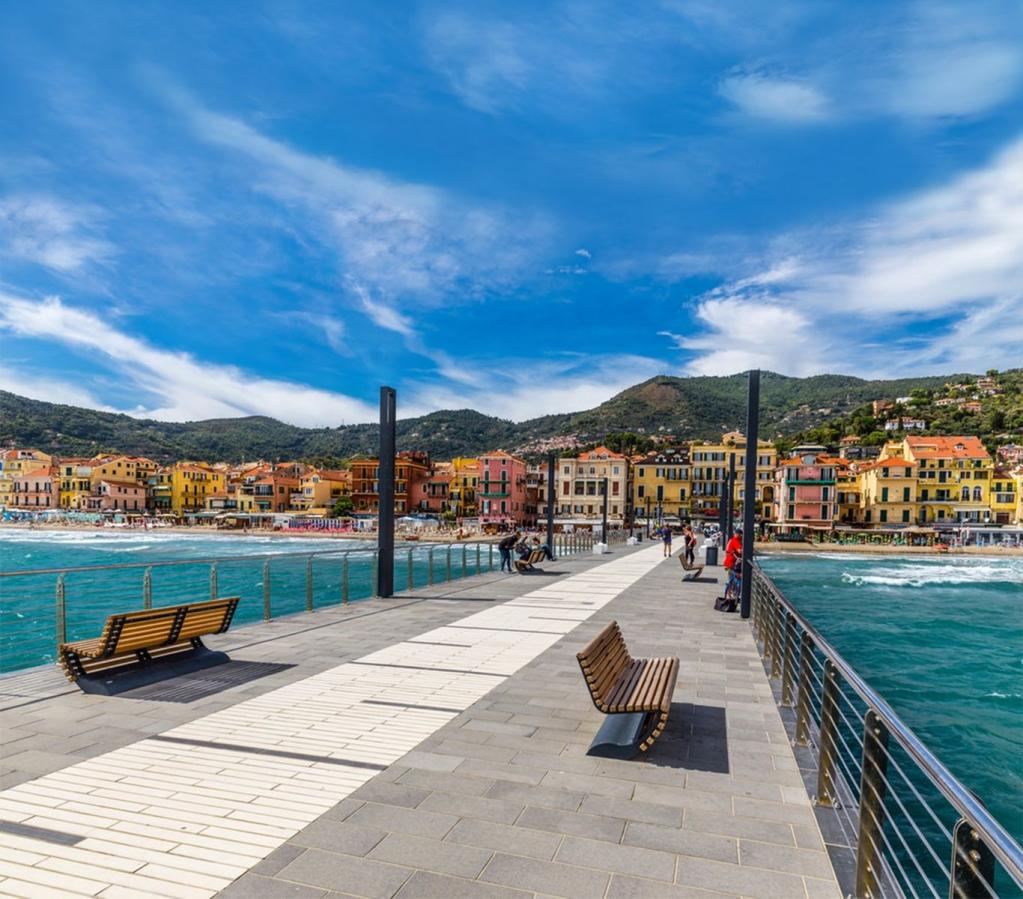 Blumenriviera_Alassio, Brücke mit Bank und Blumen über dem Wasser