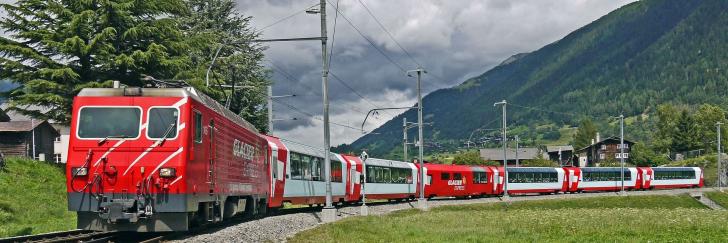 Glacier Express Zug auf Schienen hinter Bergen und grüner Landschaft